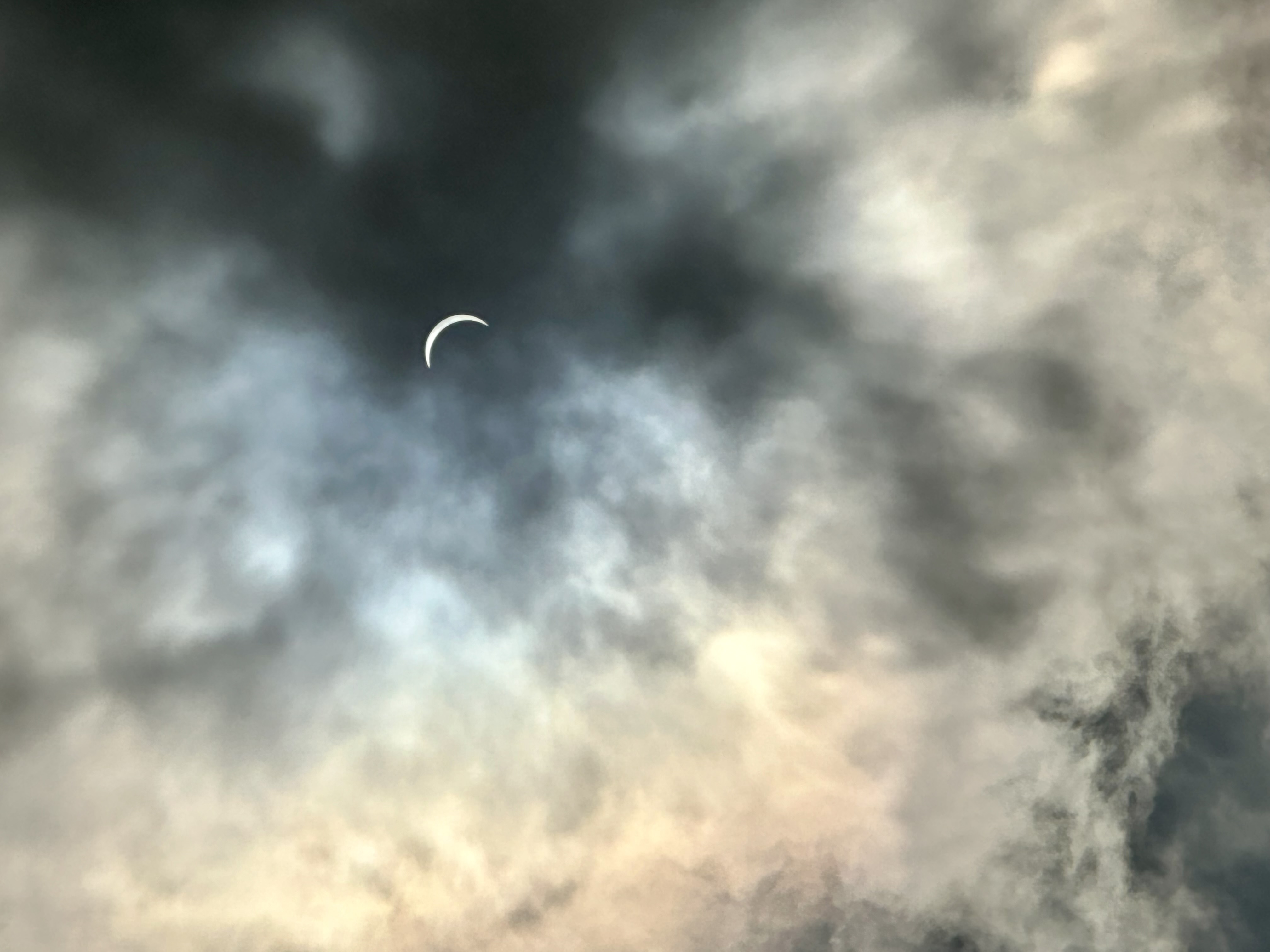 Partial solar eclipse with crescent sun visible through thick cloud cover showing golden and gray tones