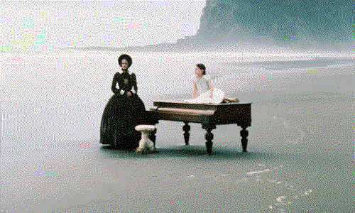 A mother and daughter stand near a piano on a beach in a still from The Piano.