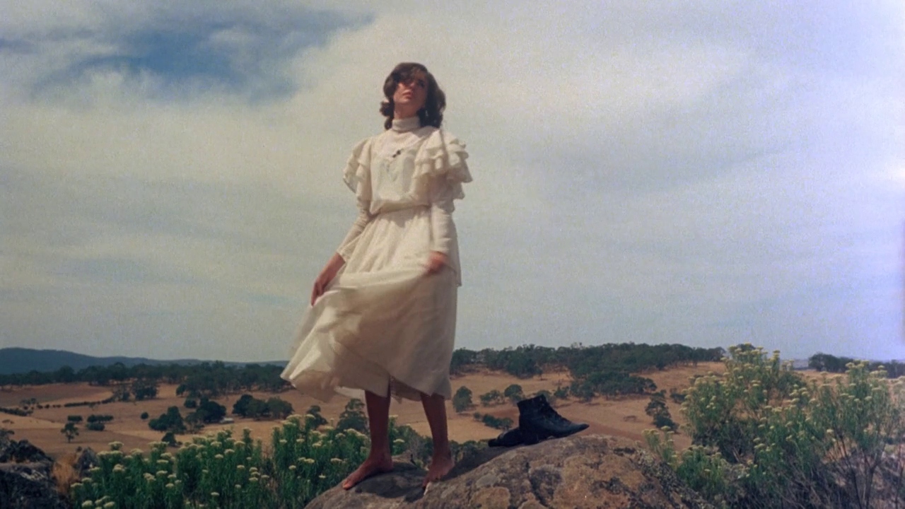 A girl dressed in Victorian clothing stands atop a rock formation.